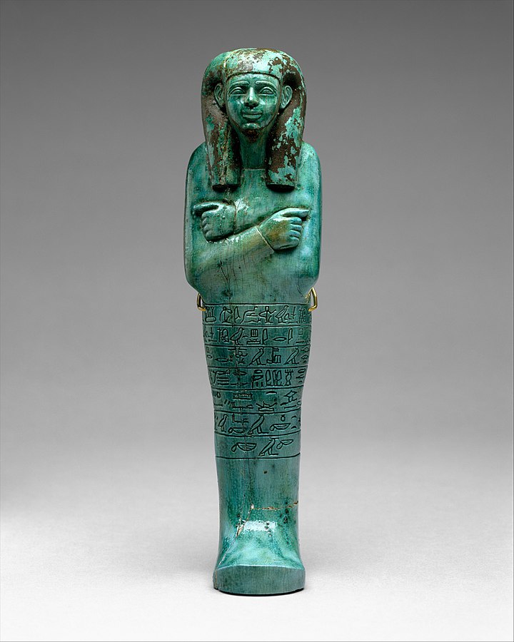 A photo of shabti, a humanoid mummiform figurine in a turquoise-ish color.